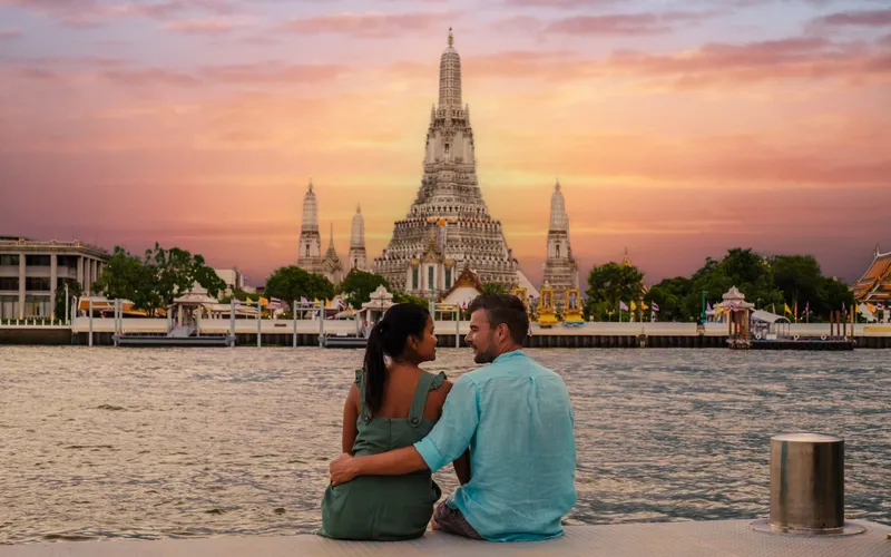 A couple watching the sunset behind Wat Arun across the Chao Phraya river in Bangkok